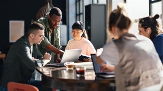5 individuals sitting at a table looking at a laptop