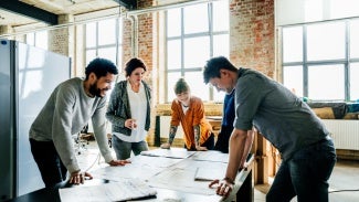Group of architects standing around table with blueprints