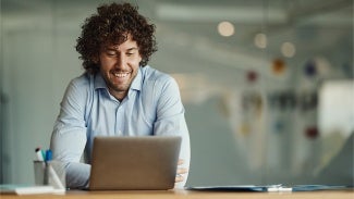 Man with curly hair and blue button up shirt working on his laptop