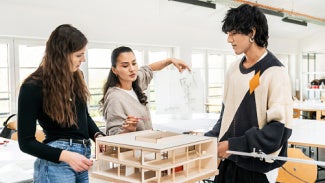 three individuals stand around a 3D architectural model within a well-lit office.